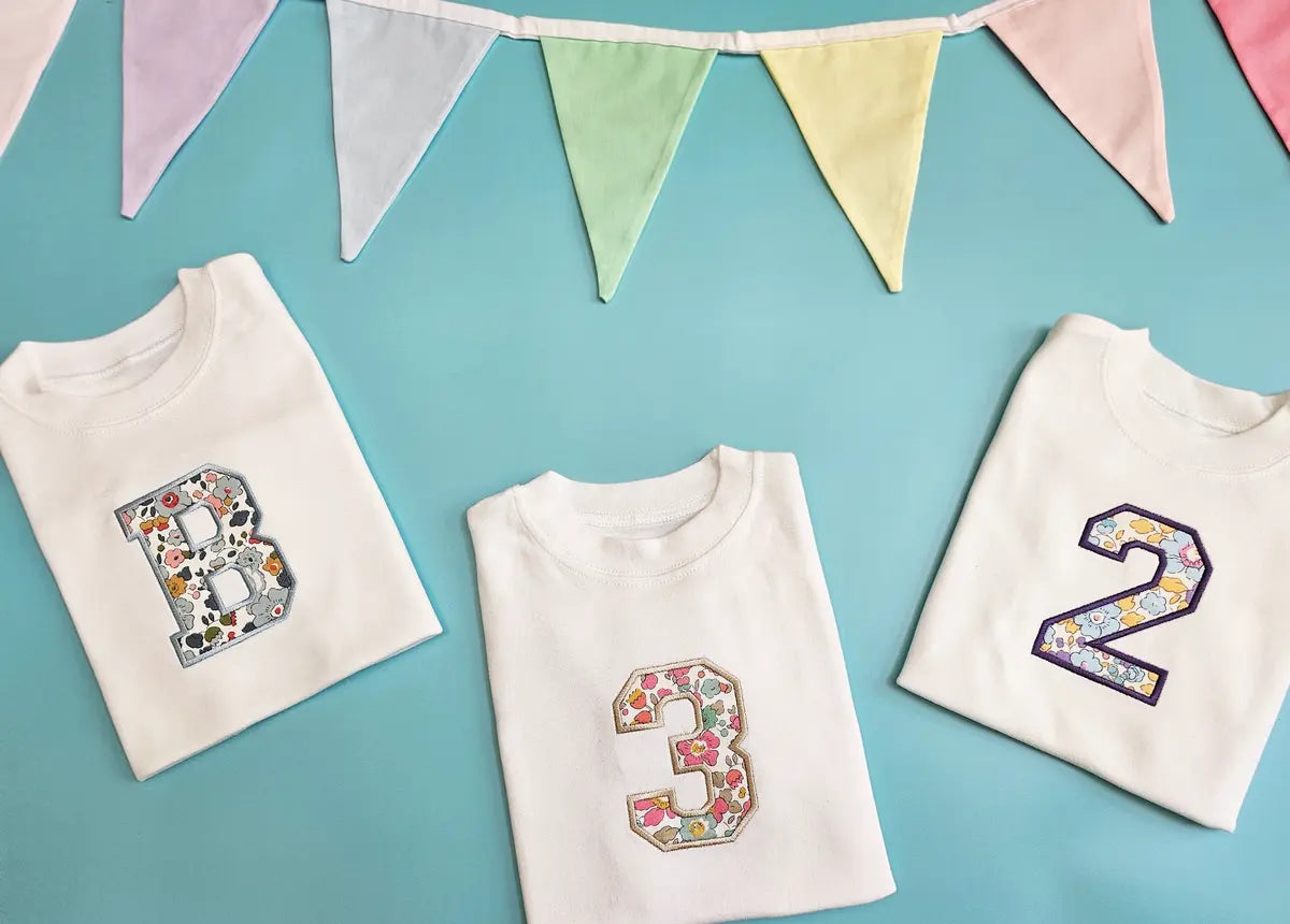 Trio of personalised embroidered birthday T‑shirts (ages 1‑5) displayed with party bunting